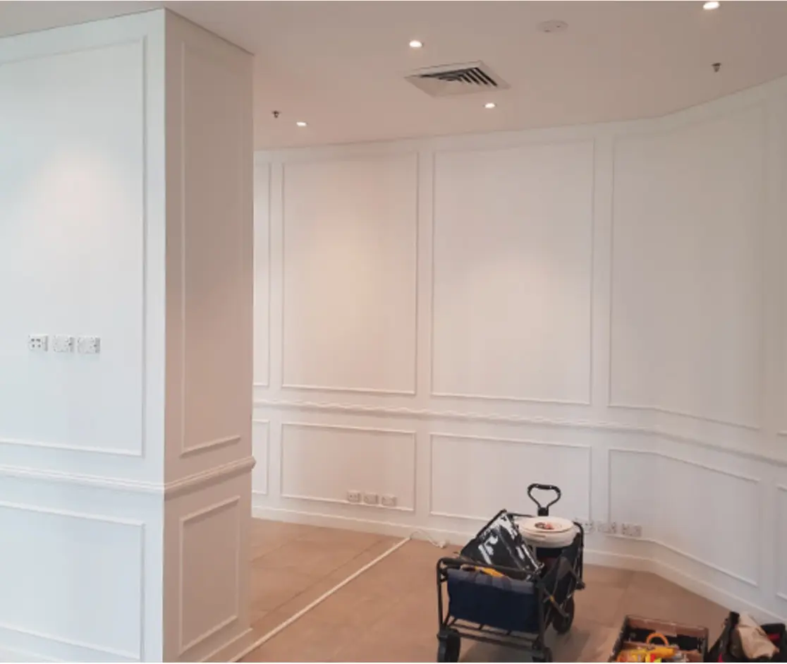 Interior renovation in progress with white walls featuring classic boiserie molding and construction tools on the floor.